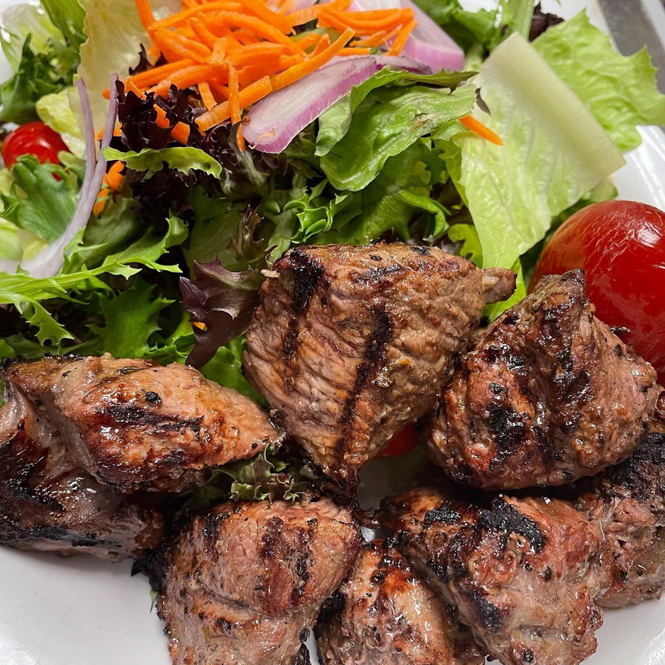 Grilled steak pieces with char marks, served alongside a fresh green salad with shredded carrots and red onion.
