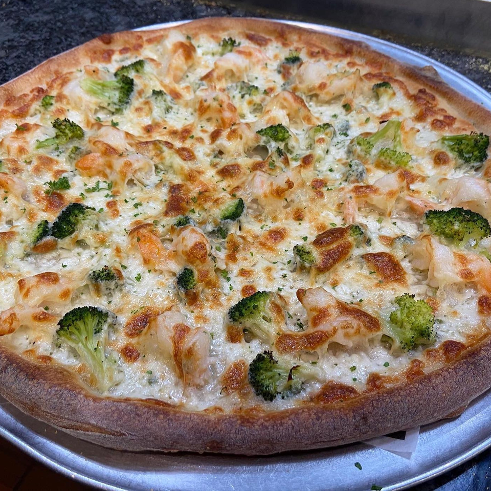 Michael G's Handcrafted Italian pizza with white sauce, broccoli, and shrimp on a metal tray.